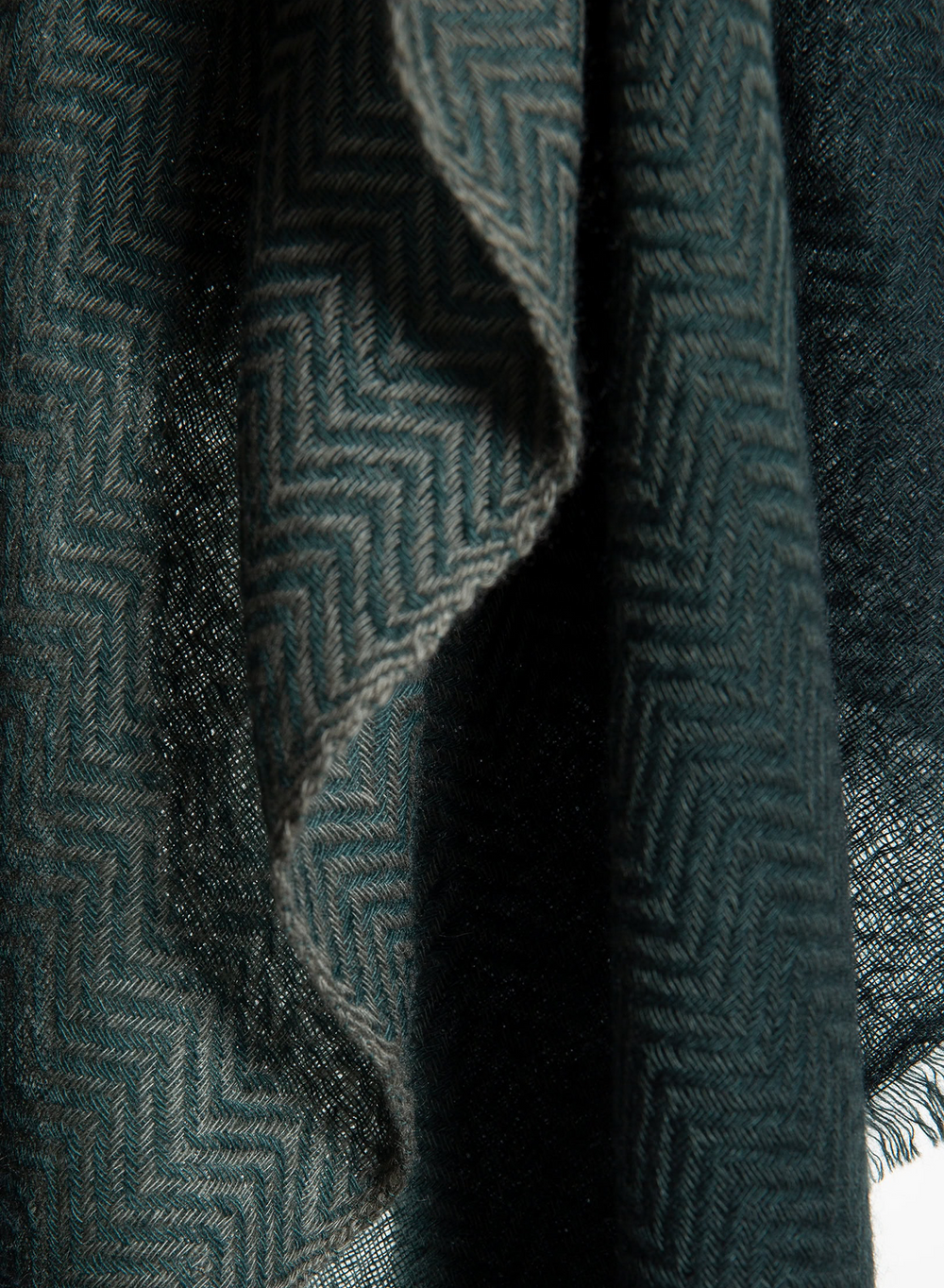 A close-up of a dark teal-green woven textile with a subtle herringbone pattern and soft draped folds.
