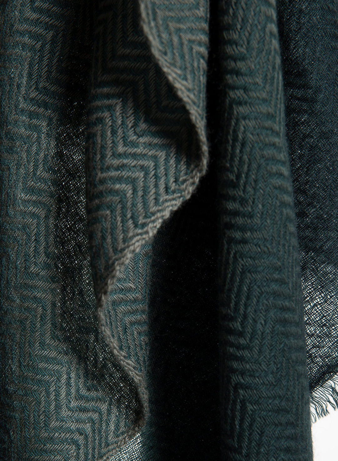 A close-up of a dark teal-green woven textile with a subtle herringbone pattern and soft draped folds.