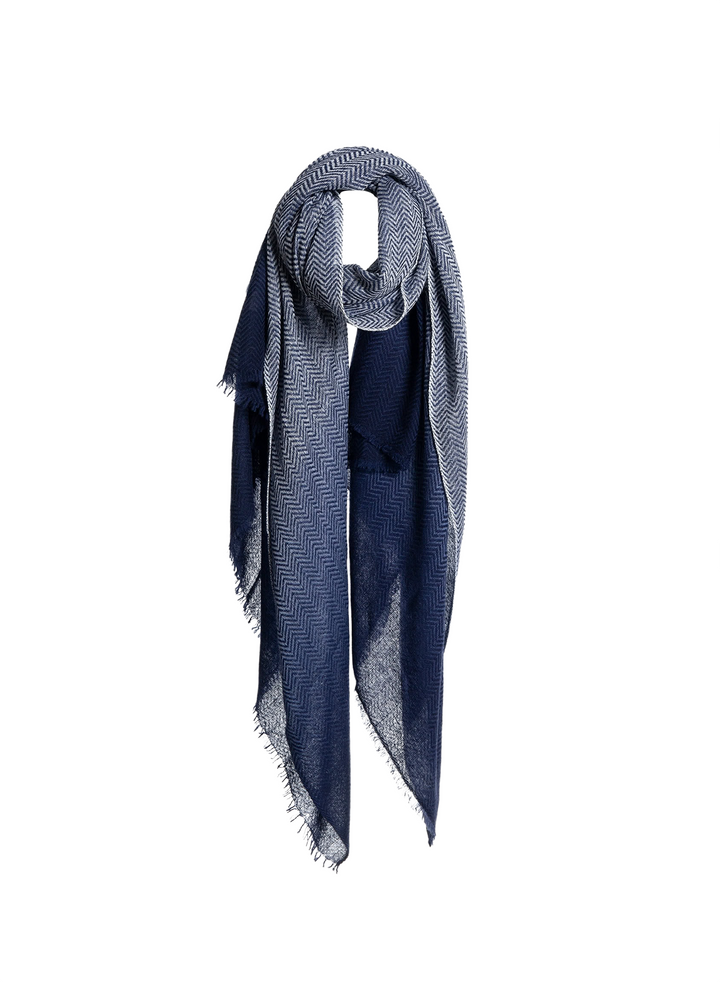 A navy blue and gray herringbone patterned scarf with fringed edges, styled in a loop on a plain white background.
