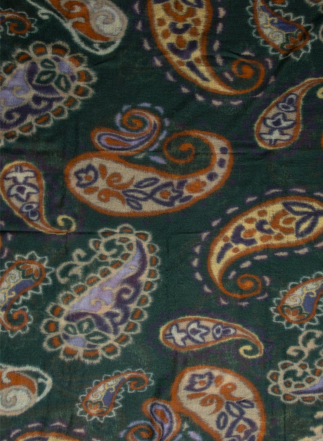 A close-up of a paisley patterned fabric with a dark green background and motifs in orange, cream, purple, and blue.