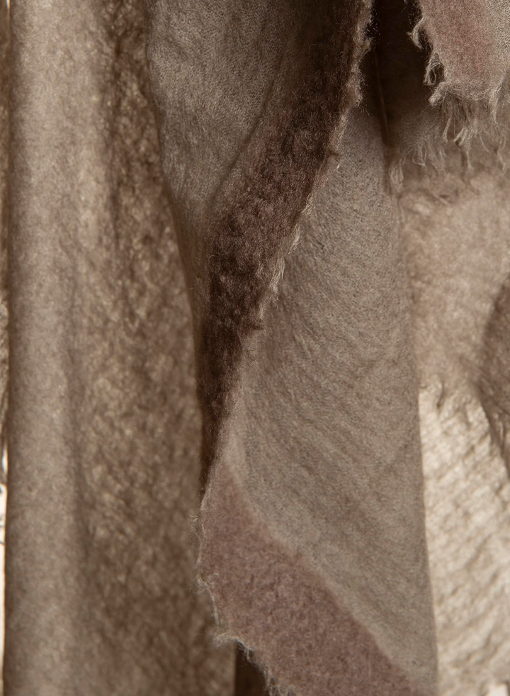 A close-up of a soft, fuzzy textile in warm taupe, beige, and dusty mauve tones with frayed edges.