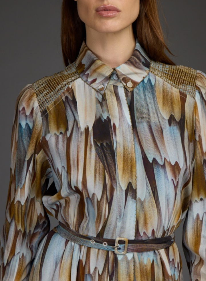 A close-up of a model wearing a long-sleeve collared shirt dress with an abstract brushstroke pattern in brown, beige, and blue, featuring a matching belt.