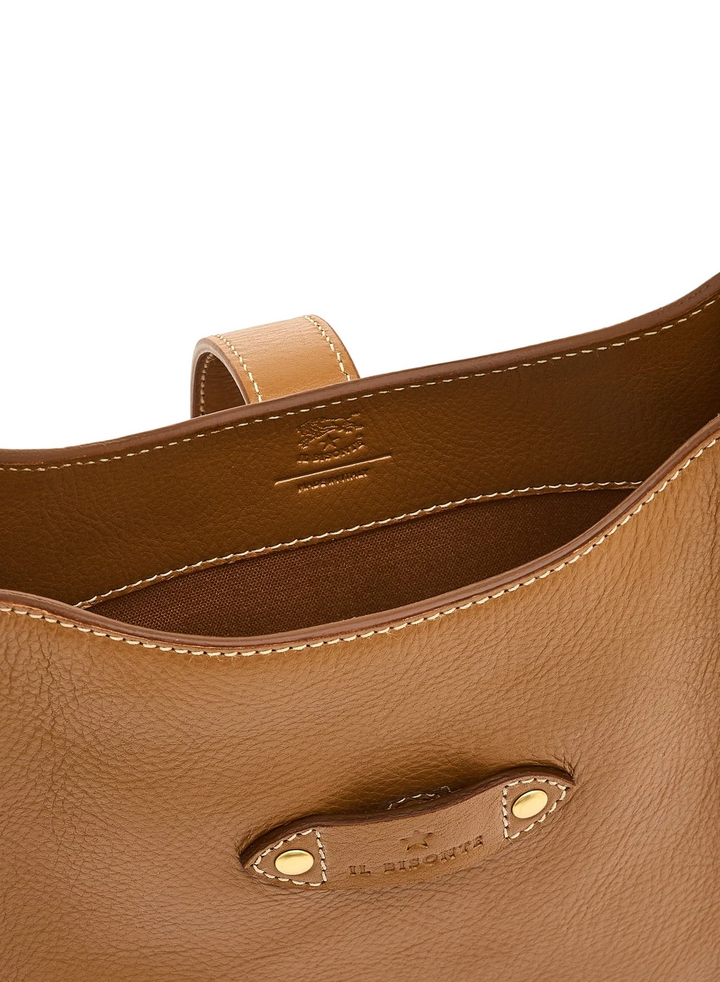 Close-up of a tan pebbled leather handbag interior showing the lining, contrast stitching, and a leather strap detail with gold-tone rivets and branding.