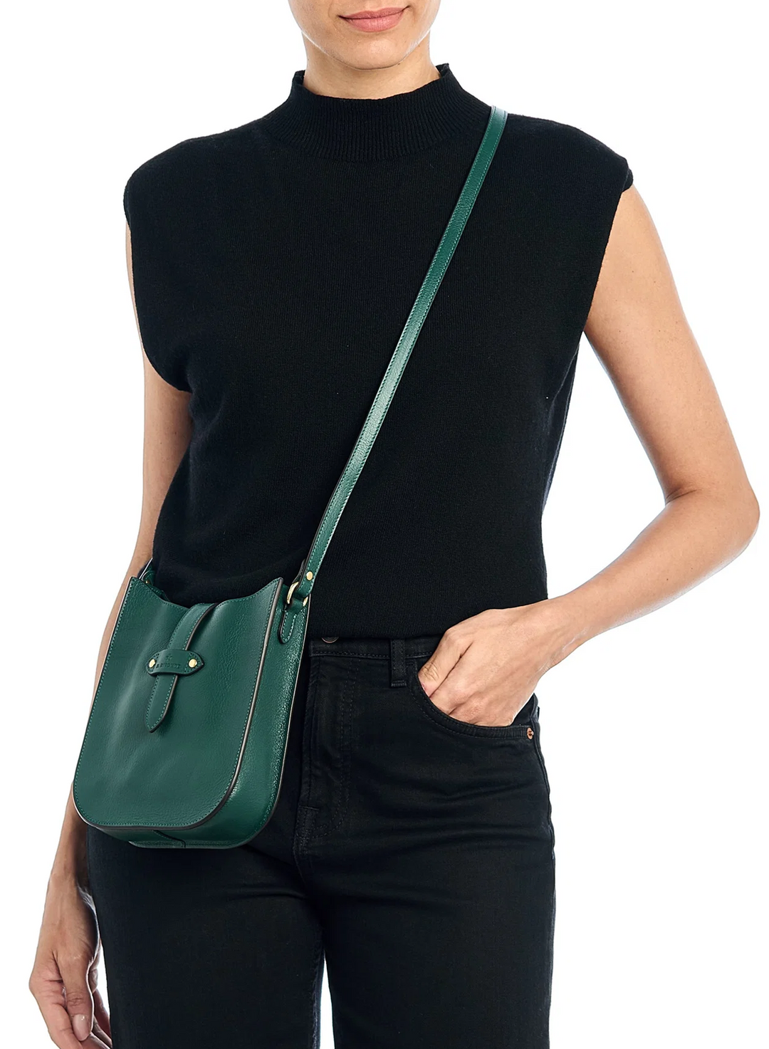A model wearing a black sleeveless mock-neck top and black jeans, carrying a dark green leather crossbody bag with a matching strap and gold-tone hardware against a white background.
