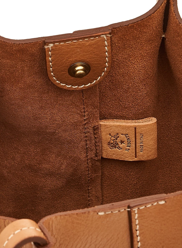 Close-up of a brown leather bag interior showing a metal snap button, stitched leather tab, and a small branded leather tag with the text &