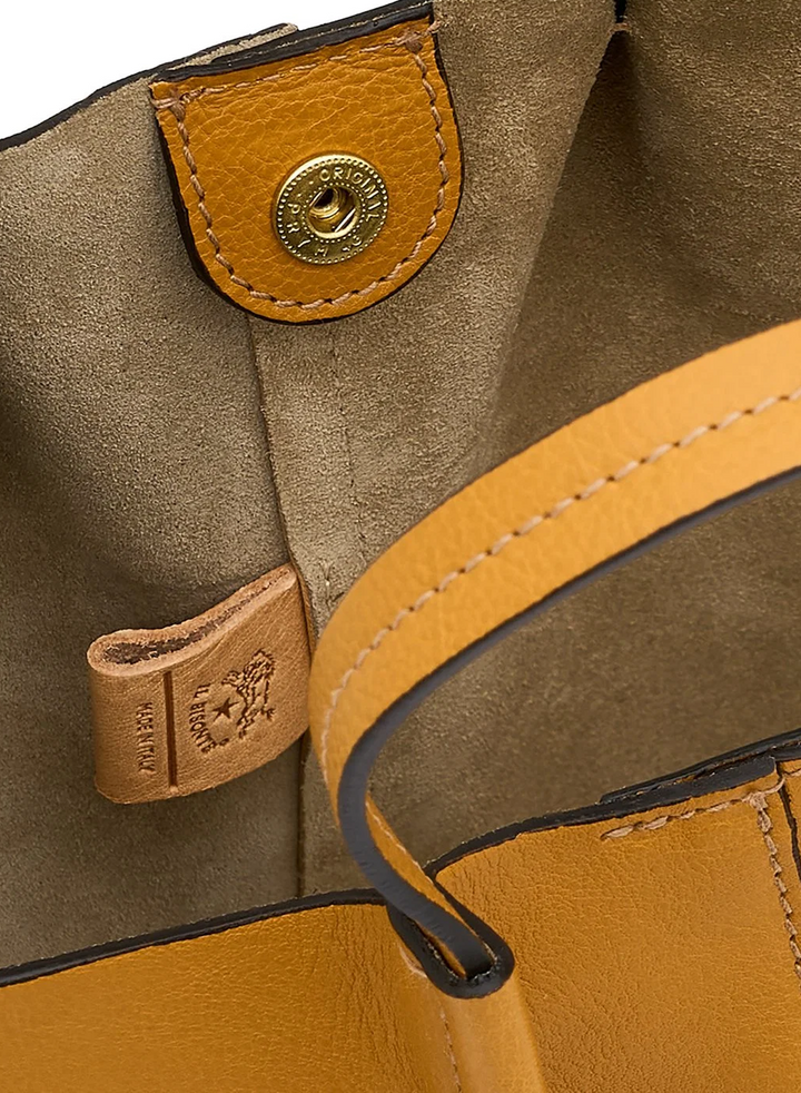Close-up detail of a tan leather handbag showing the interior lining, a gold-tone snap button, a small leather brand tab, and part of the shoulder strap.