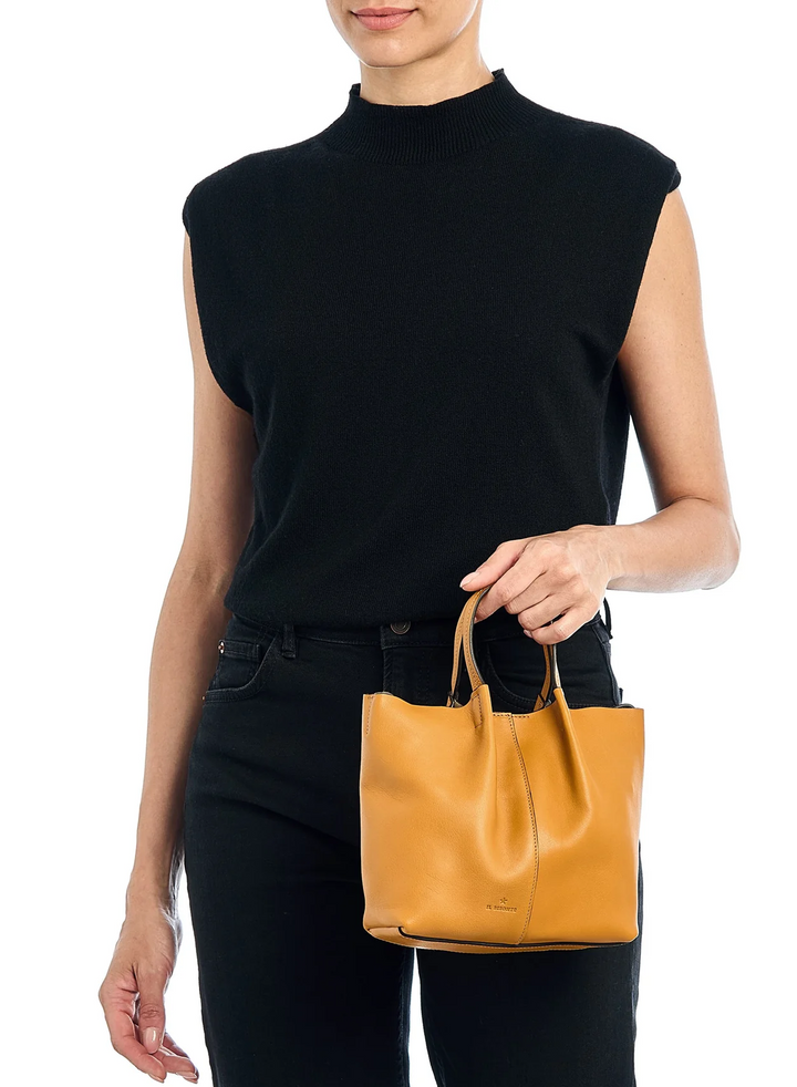 A model wearing a black sleeveless mock-neck knit top and black pants, holding a small tan leather tote bag against a plain white background.