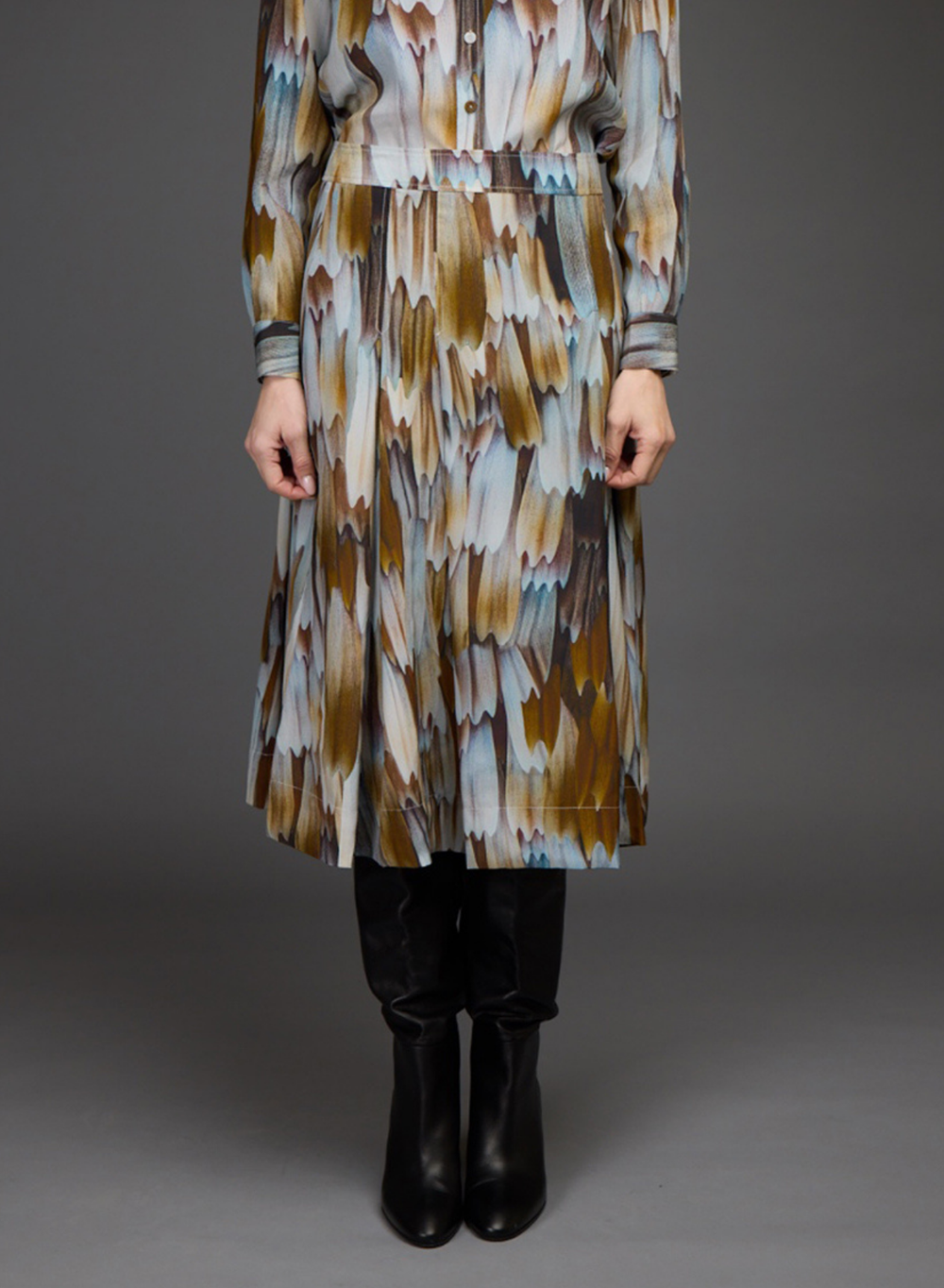 A long-sleeve midi dress with an abstract brushstroke pattern in brown, beige, and light blue, worn by a model with black boots against a dark gray studio background.