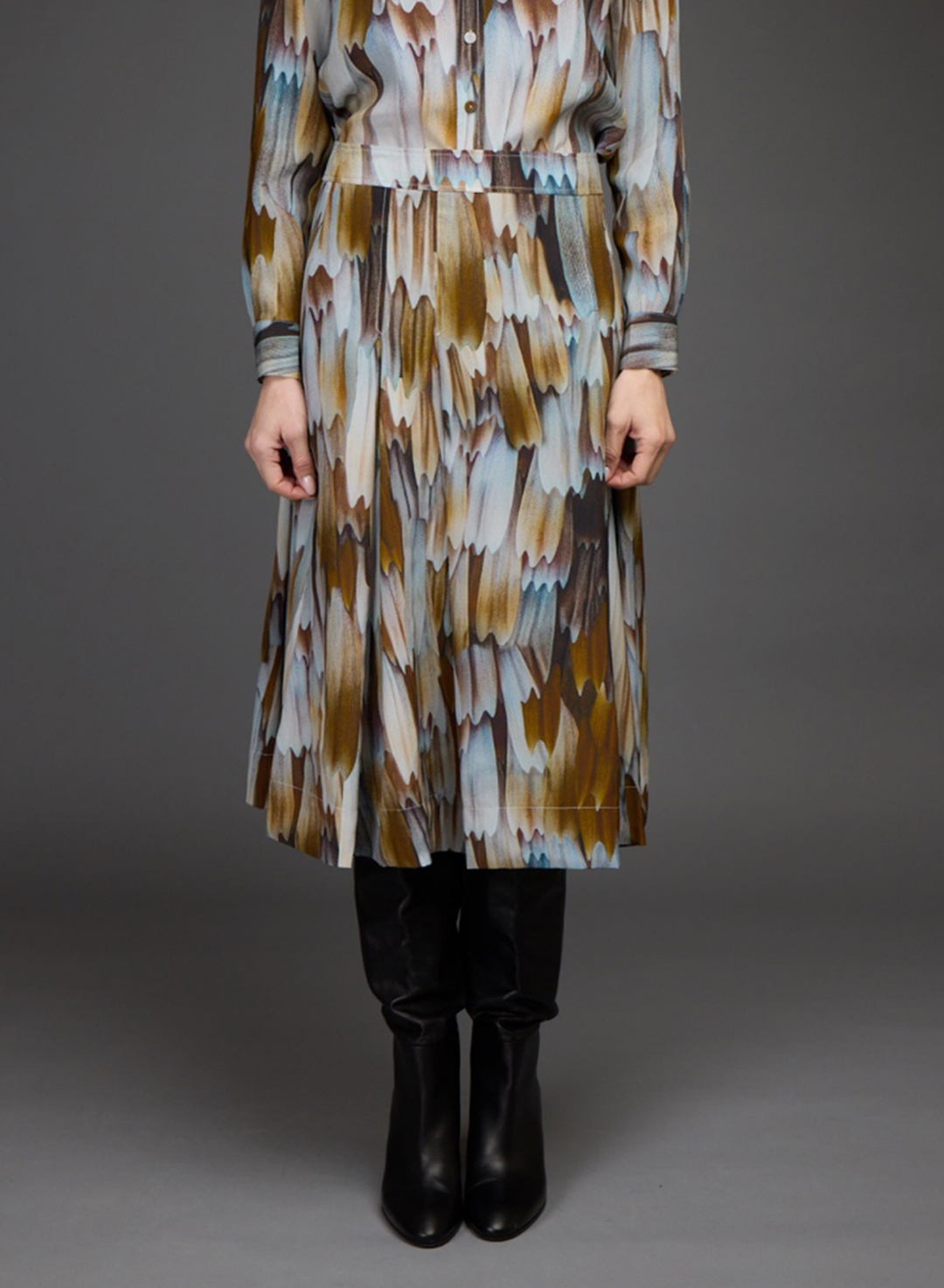 A long-sleeve midi dress with an abstract brushstroke pattern in brown, beige, and light blue, worn by a model with black boots against a dark gray studio background.
