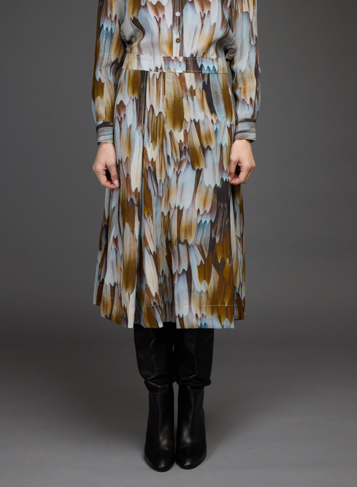 A long-sleeve midi dress with an abstract brushstroke pattern in brown, beige, and light blue, worn by a model with black boots against a dark gray studio background.