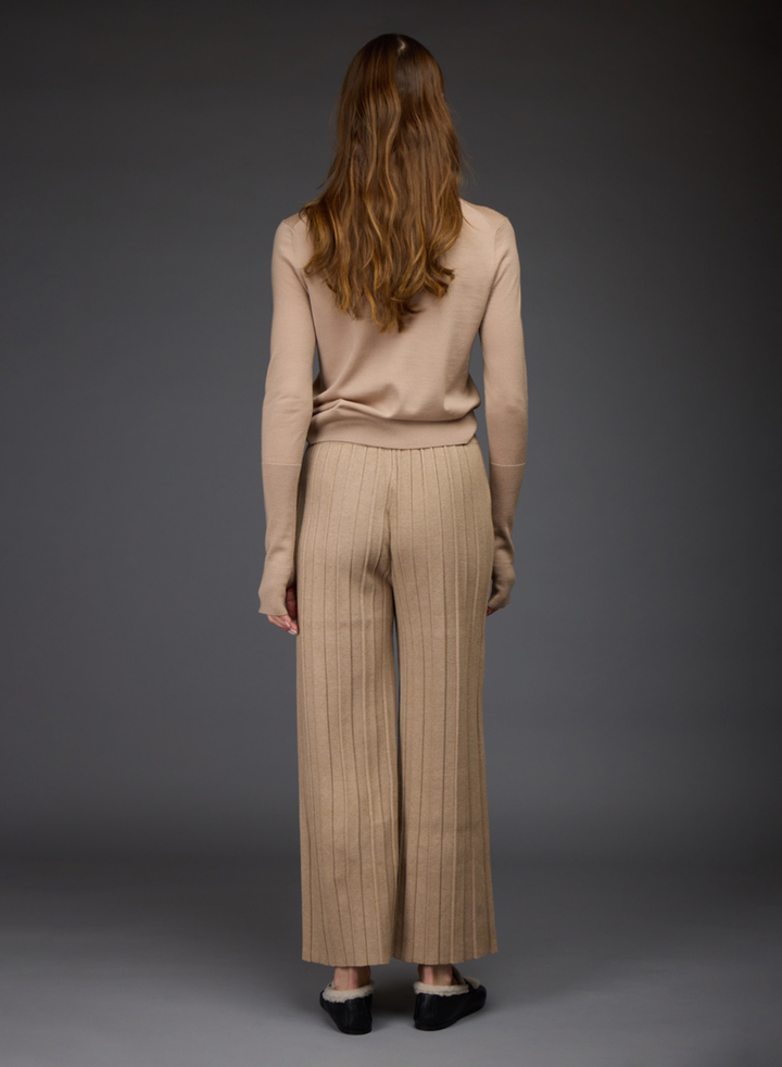 A woman viewed from the back wearing a beige ribbed turtleneck sweater by Love Binetti and matching wide-leg drawstring pants paired with black and white loafers.